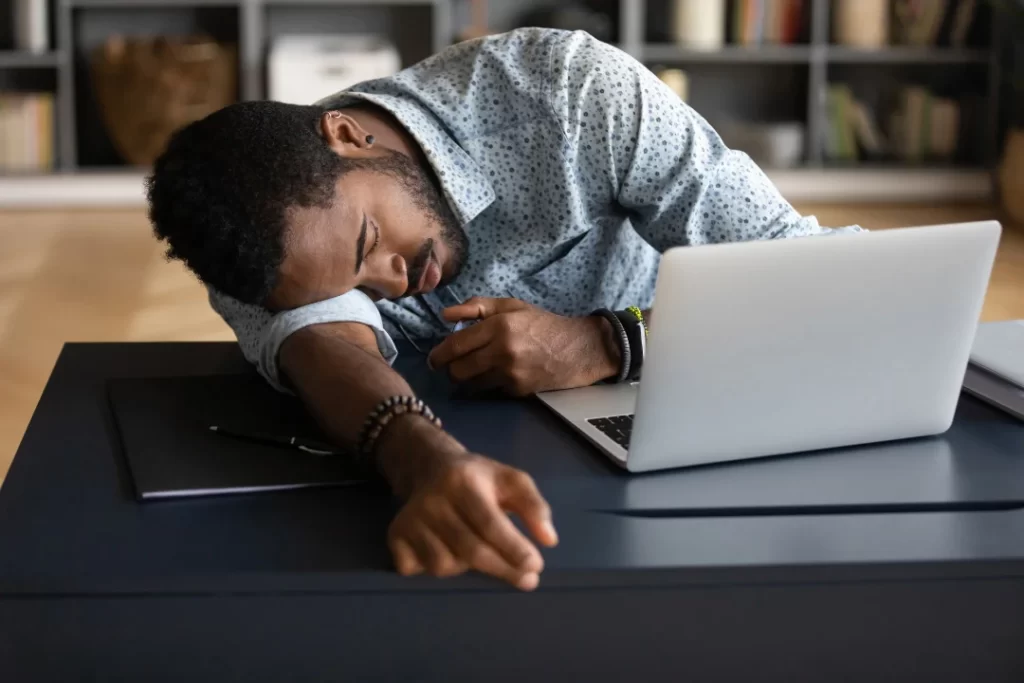 A black guy sleeping at work in front of his laptop. 