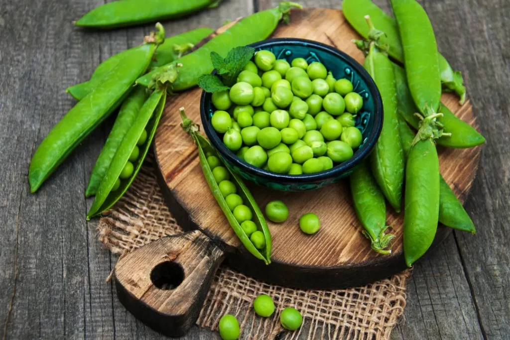 Fresh and organic green peas in a bowl on wooden board.